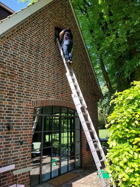 Fensterputzer auf der Anlegeleiter reinigt ein hohes Giebelfenster