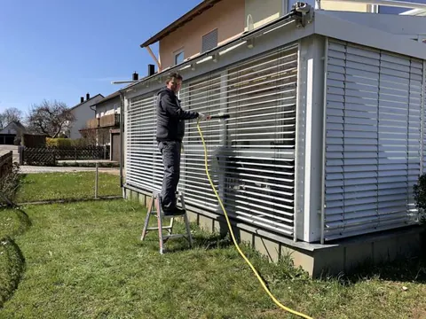 Fensterputzer reinigt die Raffstores eines Wintergartens mit wasserführender Bürste