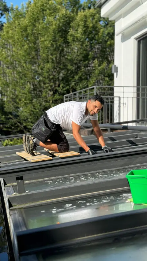 Soubhi Hussein kniet auf Trittbrettern und reinigt ein Terrassendach aus Glas